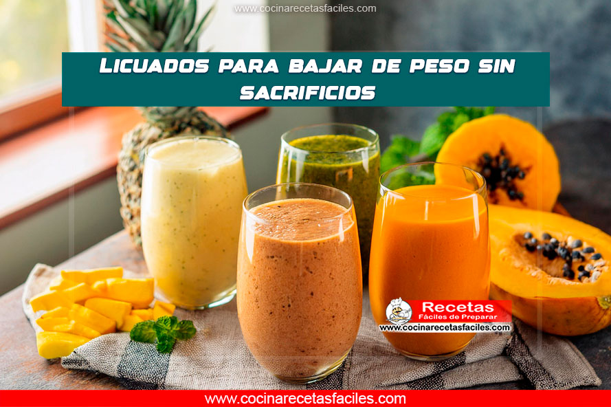 Una variedad de licuados para bajar de peso hechos con papaya, piña, mango y pepino, servidos en vasos transparentes y rodeados de rodajas de frutas frescas y hierbas, sobre una mesa de cocina de madera.
