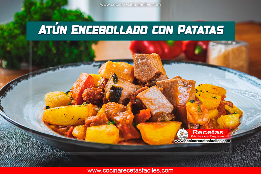 Atún en cubos dorados con cebolla caramelizada, pimientos verdes fritos y patatas cocidas y doradas, servido en una mesa de madera.
