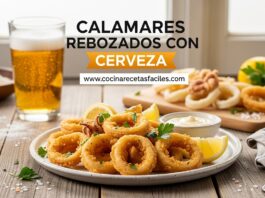 Plato de calamares rebozados con cerveza dorados y crujientes servidos en plato blanco rústico sobre mesa de madera, acompañados de limón fresco, perejil y salsa alioli, con vaso de cerveza fría al fondo