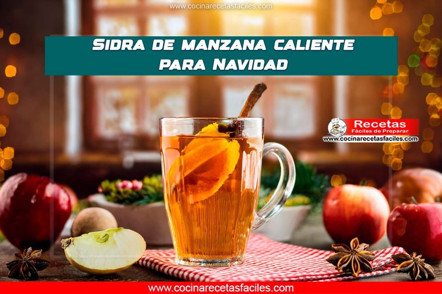 Sidra de manzana caliente servida en vaso transparente, decorada con rodajas de manzana, naranja y una ramita de canela, en un fondo navideño cálido.