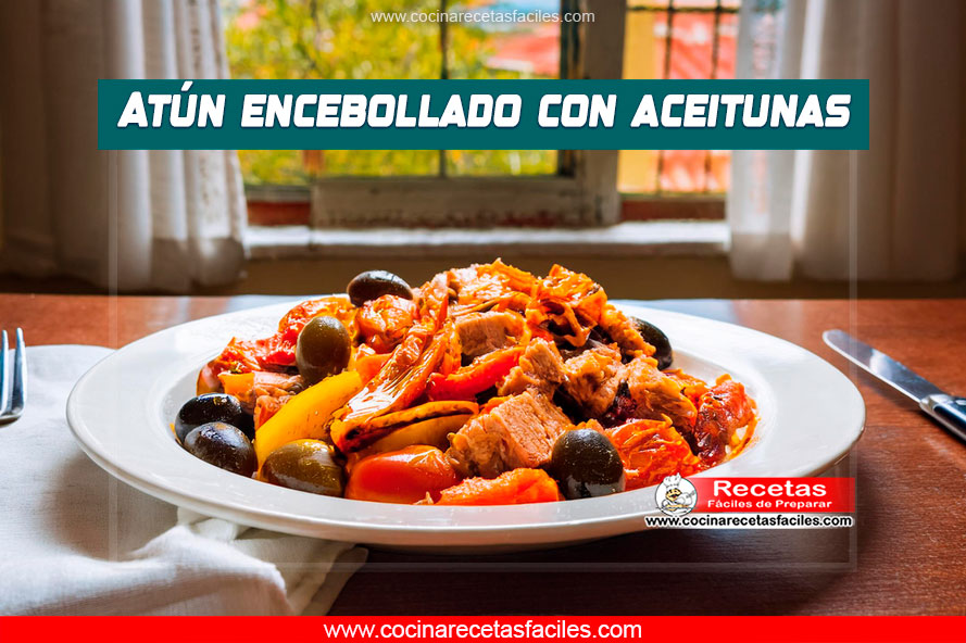 "Atún encebollado con aceitunas, cebollas caramelizadas, pimientos y tomates, servido en una sartén sobre una mesa de madera."