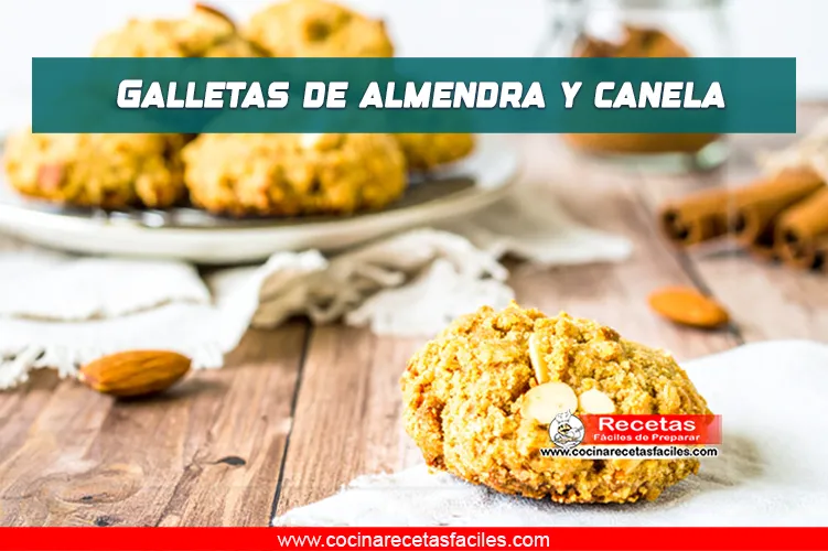 Galletas caseras de almendra y canela sobre una mesa de madera con mantel, en una cocina con ventana grande, algunas decoradas con almendras laminadas.