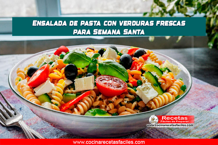 "Ensalada fresca de pasta con tomate cherry, pepino, zanahoria, pimiento rojo, cebolla morada, aceitunas, aguacate y albahaca, servida en una mesa de madera con mantel en una cocina luminosa."